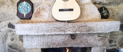 Een stenen open haard met een gitaar, een klok en twee flessen op een plank erboven.