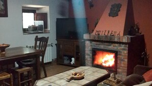 A cozy living room with a fireplace, a dining table, and a TV. - Casa Florentina (Cabrales)