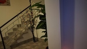 Una escalera con barandilla metálica, una planta en maceta y una lámpara de pared encendida.