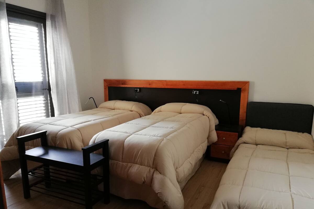 A room with two beds, a small table, and a window with curtains.