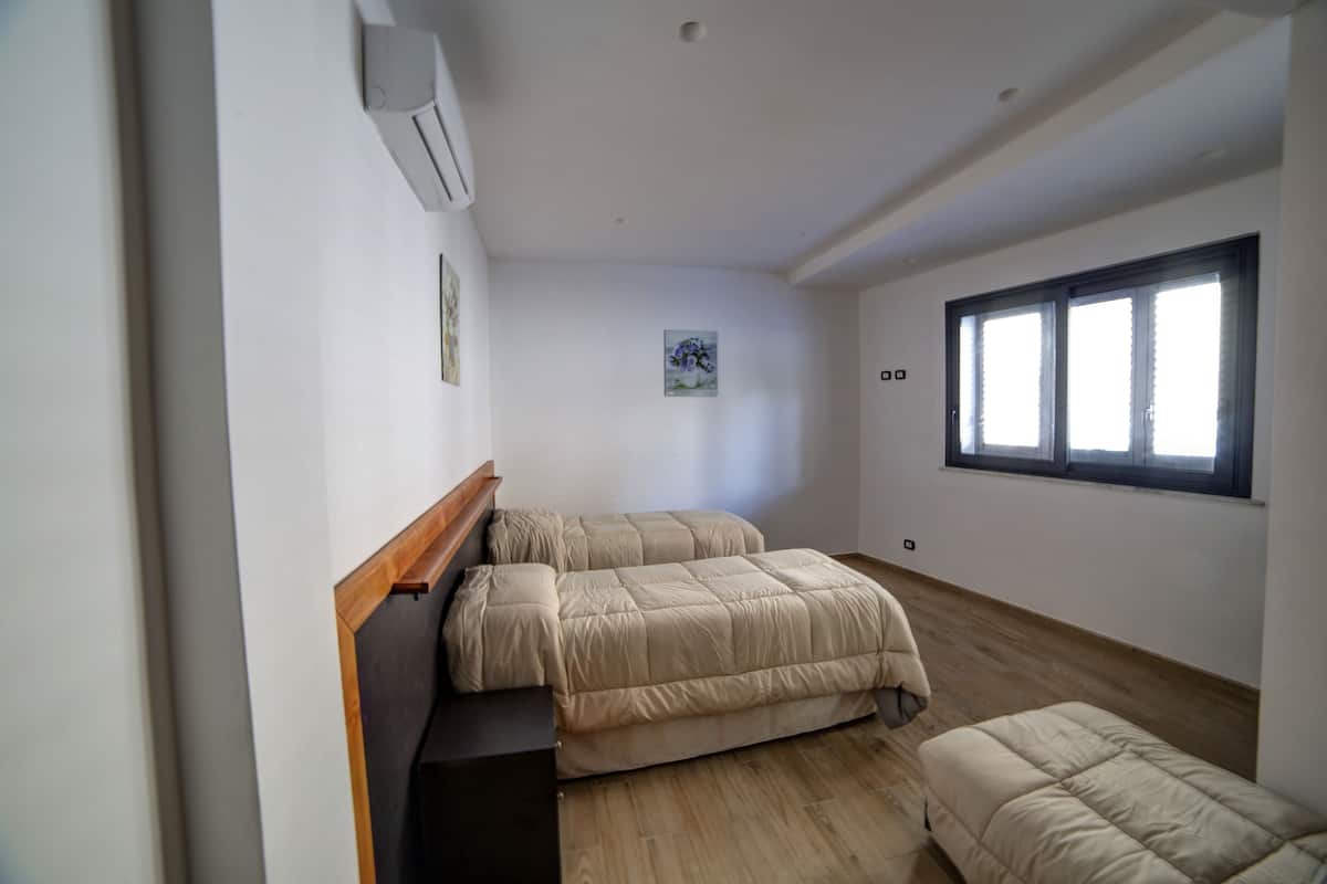 A bedroom with two beds, a wooden headboard, a small window, and a wall-mounted air conditioner.