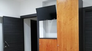 Una habitación con un armario de madera, un televisor negro encima y una cama blanca.