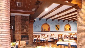 Un restaurant aux murs de briques, aux poutres apparentes et aux sols carrelés. Les tables sont recouvertes de nappes blanches et les chaises sont en bois.