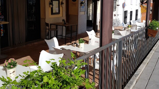 Un café en plein air avec des tables et des chaises blanches, une clôture en bois et des plantes en pot.