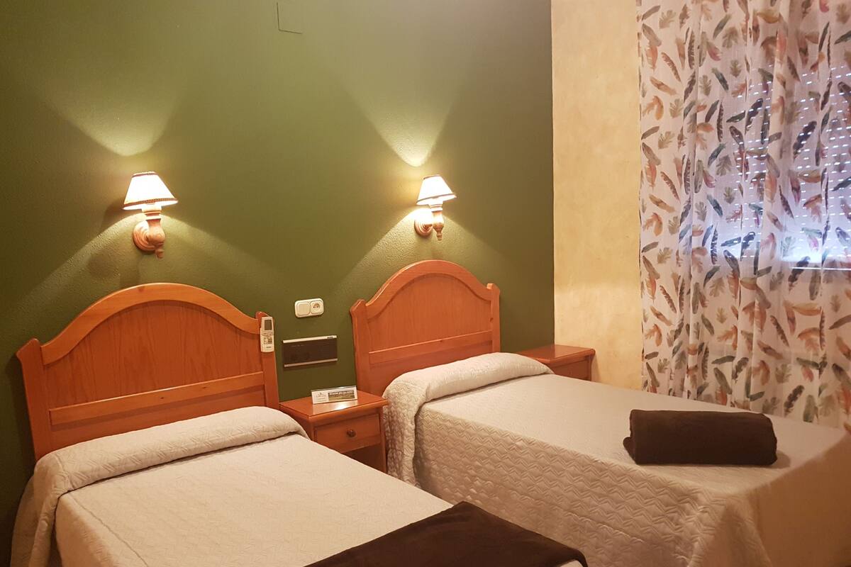 Une chambre d’hôtel avec deux lits simples, chacun doté d’une tête de lit en bois, de tables de chevet et de lampes fixées au mur.