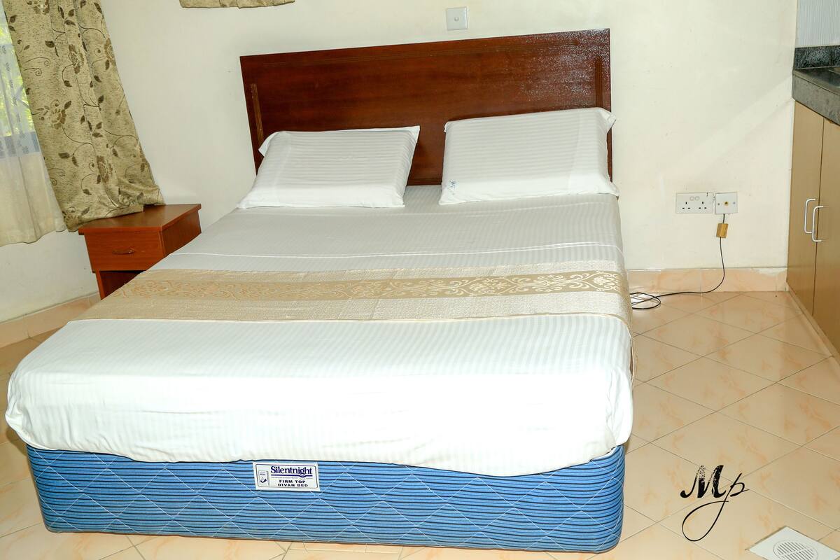 A neatly made bed with a wooden headboard, a bedside table, and a power outlet on the wall.