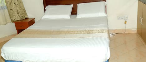 A neatly made bed with a wooden headboard, a bedside table, and a power outlet on the wall.
