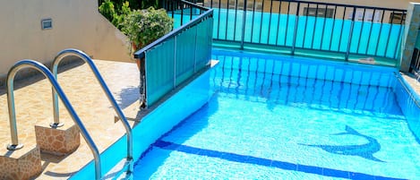 Una piscina con agua azul cristalina, escaleras metálicas y un borde con baldosas.