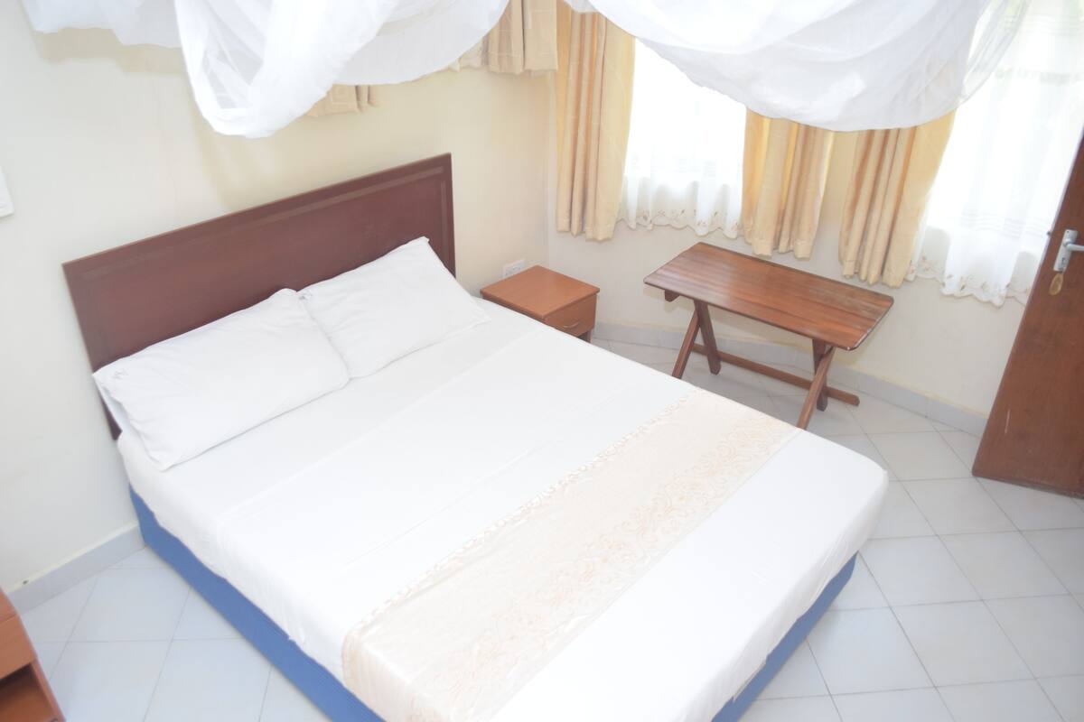 A neatly made bed with white linens, a wooden headboard, and a bedside table with a lamp.
