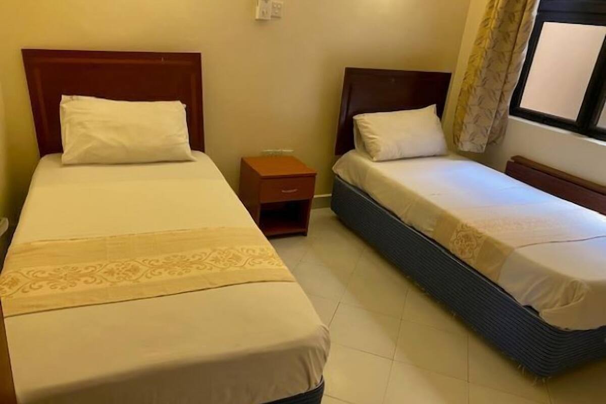 A twin room with two single beds, a small wooden nightstand, and a window with curtains.