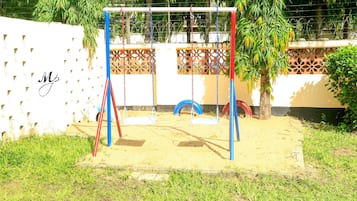 Children can play on the swing set and tire swing in this outdoor playground surrounded by grass and a sandy area.