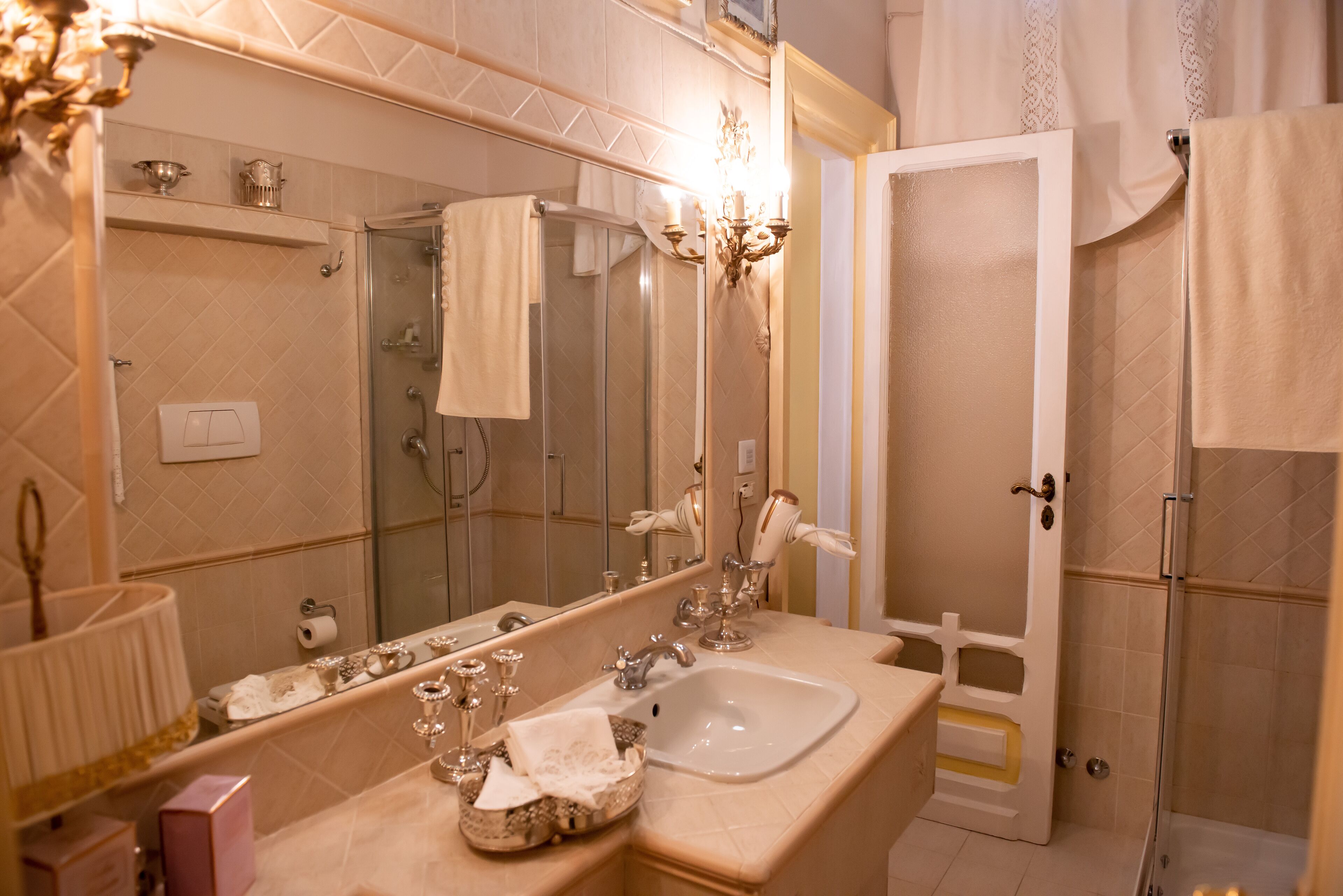 A bathroom with a large mirror, a sink, a shower, and a vanity with a lamp.