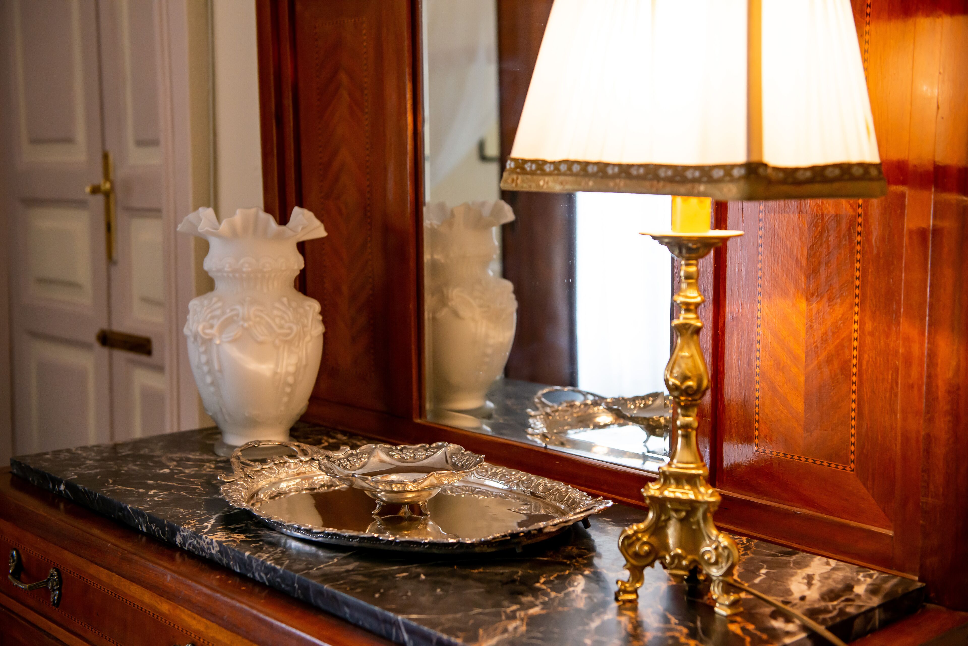 Una encimera de mármol con una bandeja decorativa, una lámpara de latón y un jarrón blanco.
