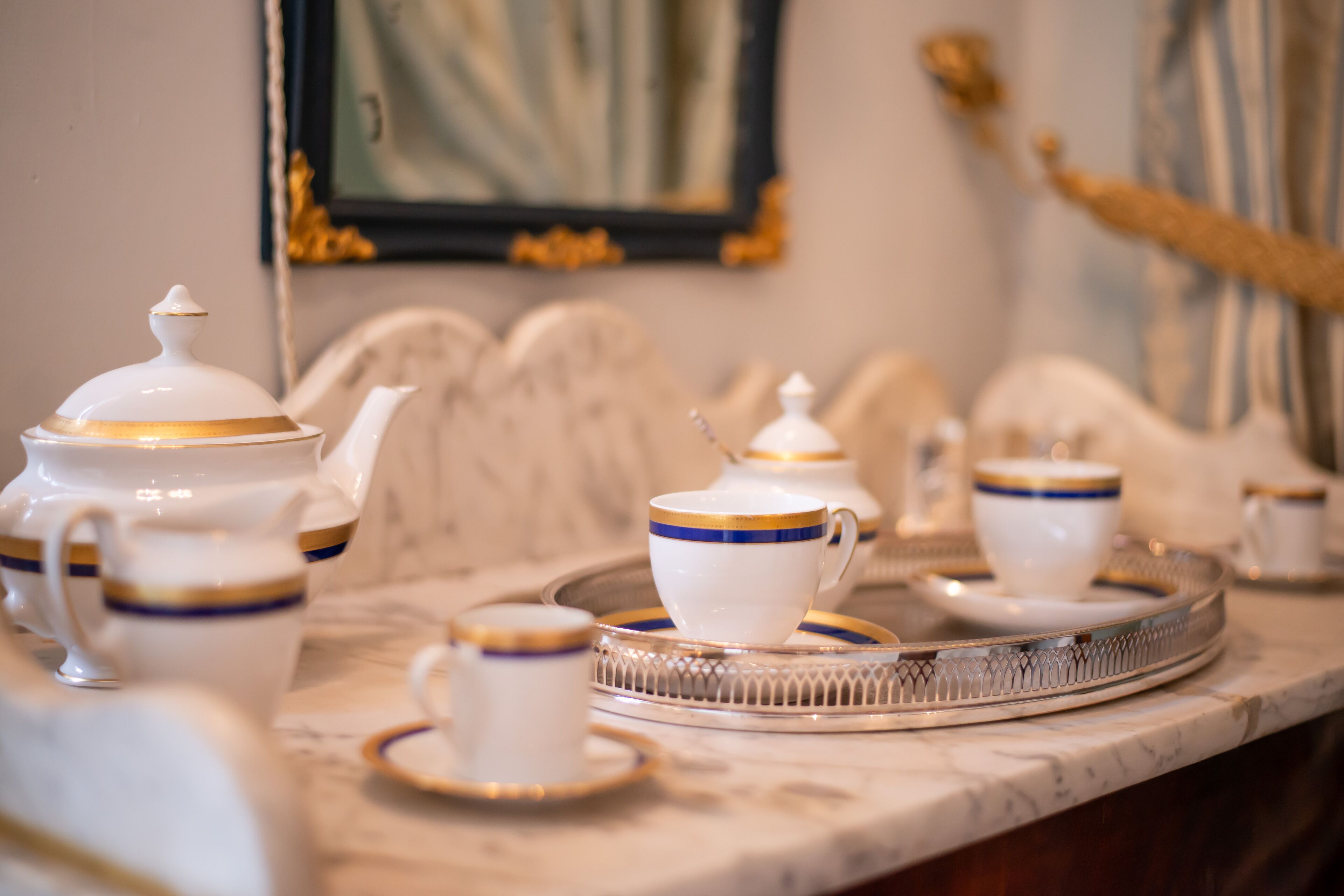 Una mesa con cubierta de mármol y teteras, tazas y platillos blancos con detalles dorados.