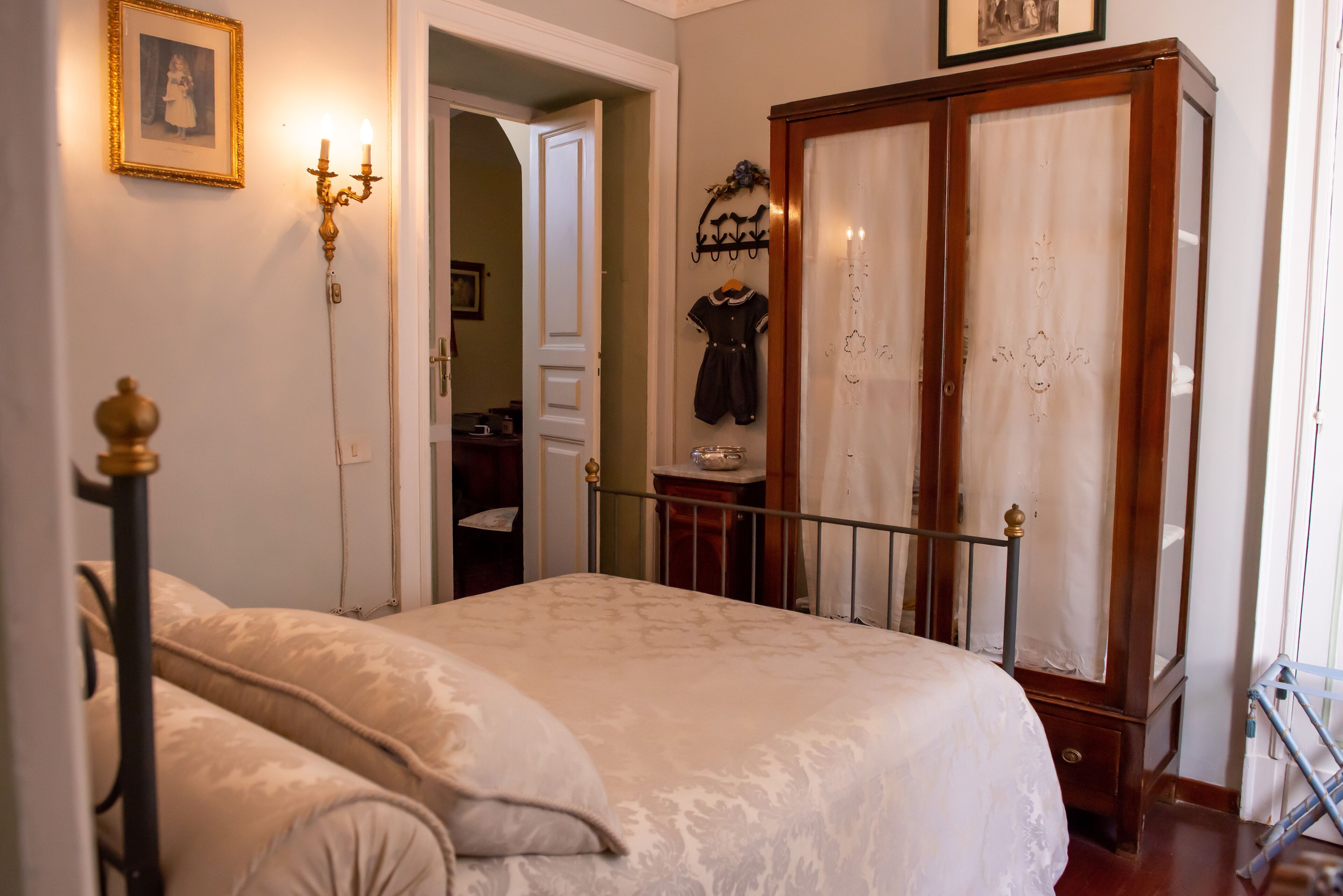 A bedroom with a bed, a wardrobe, a mirror, and a wall-mounted coat rack.