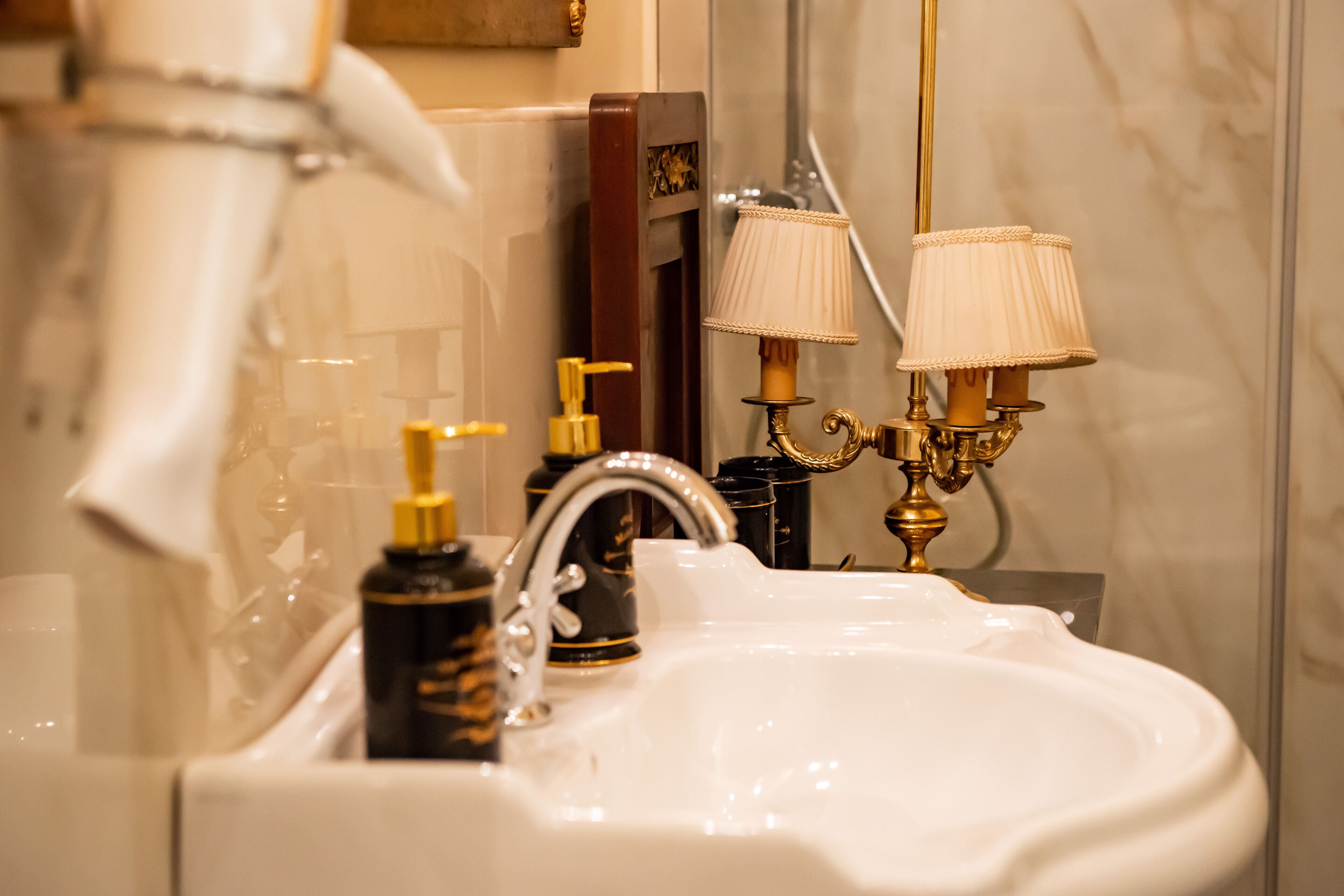 A bathroom with a white sink, gold faucets, and two wall-mounted lamps.