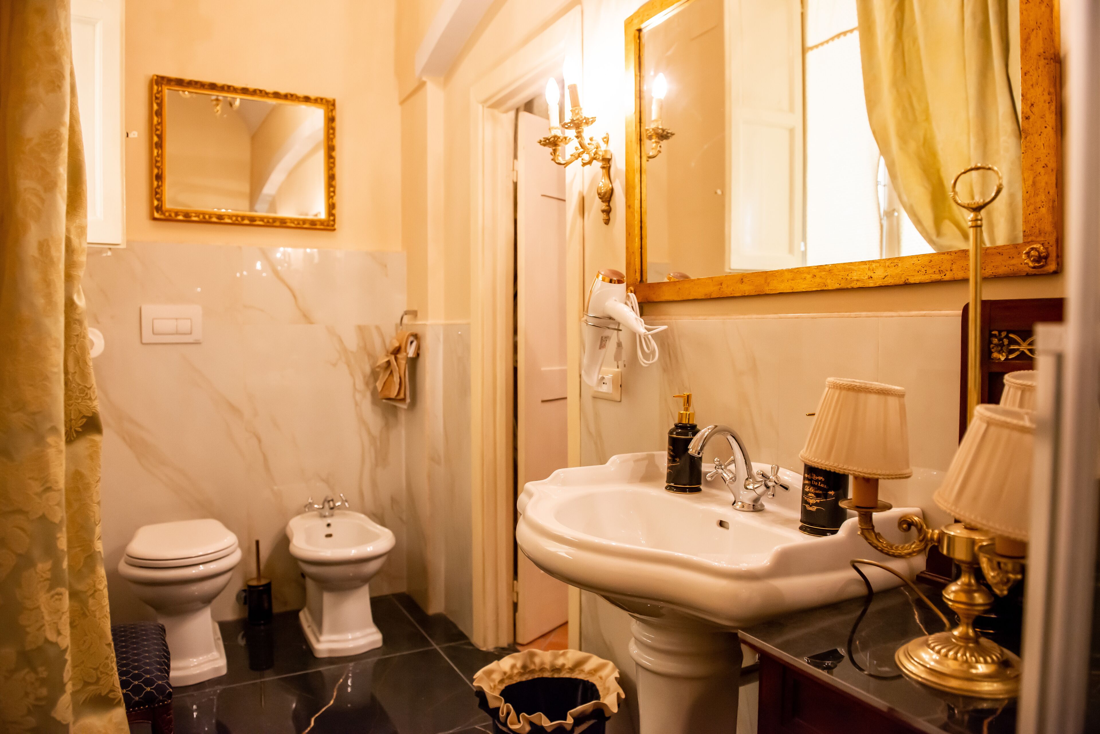 A bathroom with a white sink, two toilets, a bidet, a mirror with a gold frame, and a chandelier.