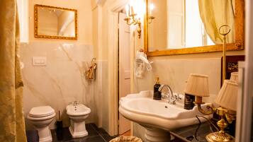 A bathroom with a white sink, two toilets, a bidet, a mirror with a gold frame, and a chandelier.
