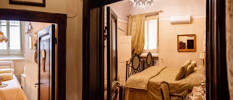 Una habitación con cama, una silla, una mesa con bandeja, un espejo y una araña.