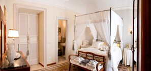 Una cama con dosel, una mesita de noche con lámpara y una silla con toallas.