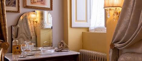A well-lit room with a vanity, mirror, framed pictures, and a lamp.
