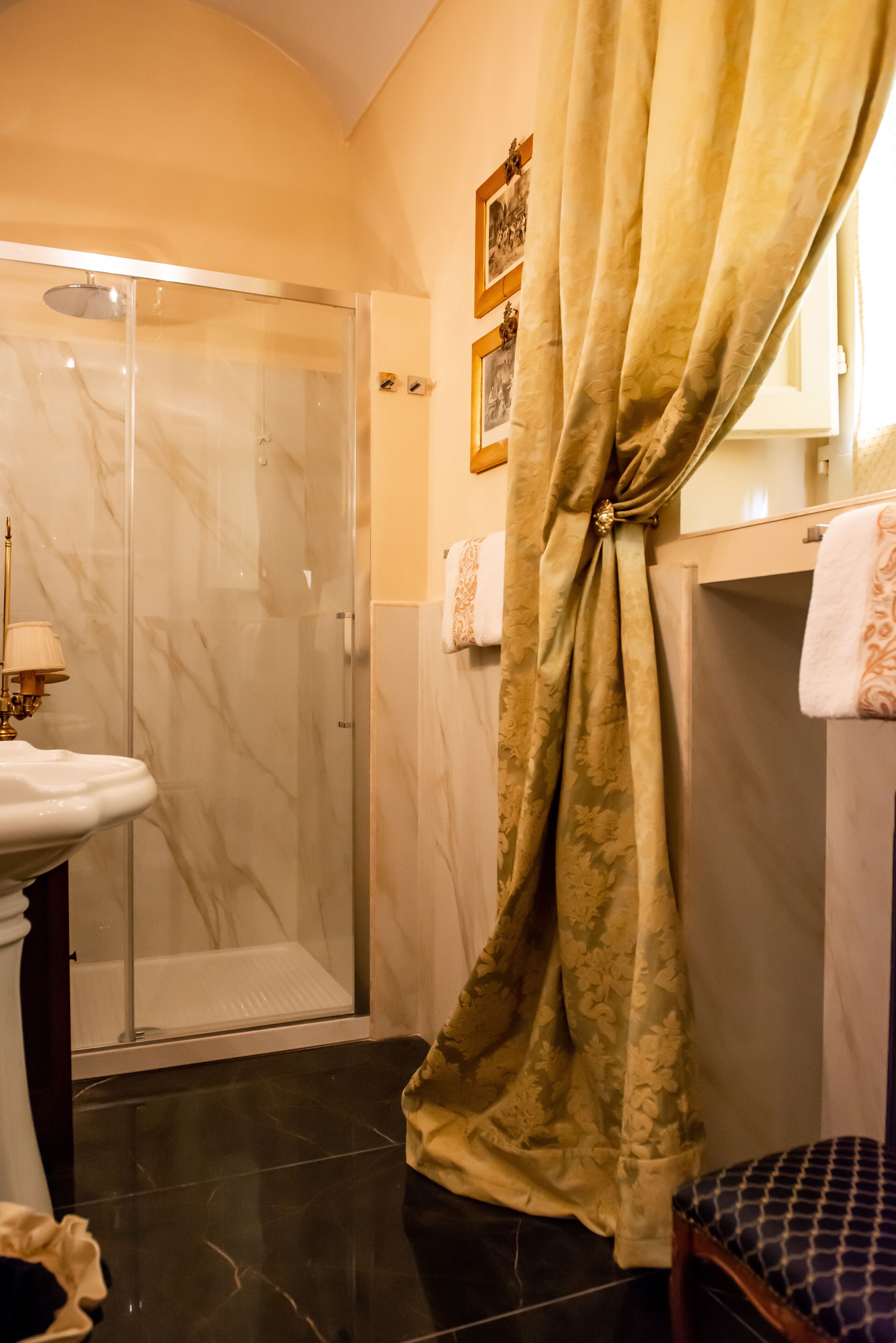 Un baño con ducha de vidrio, lavamanos de mármol y cortina estampada.