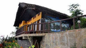 A building with a thatched roof, a balcony with a metal railing, and a mural on the wall depicting a tropical scene.