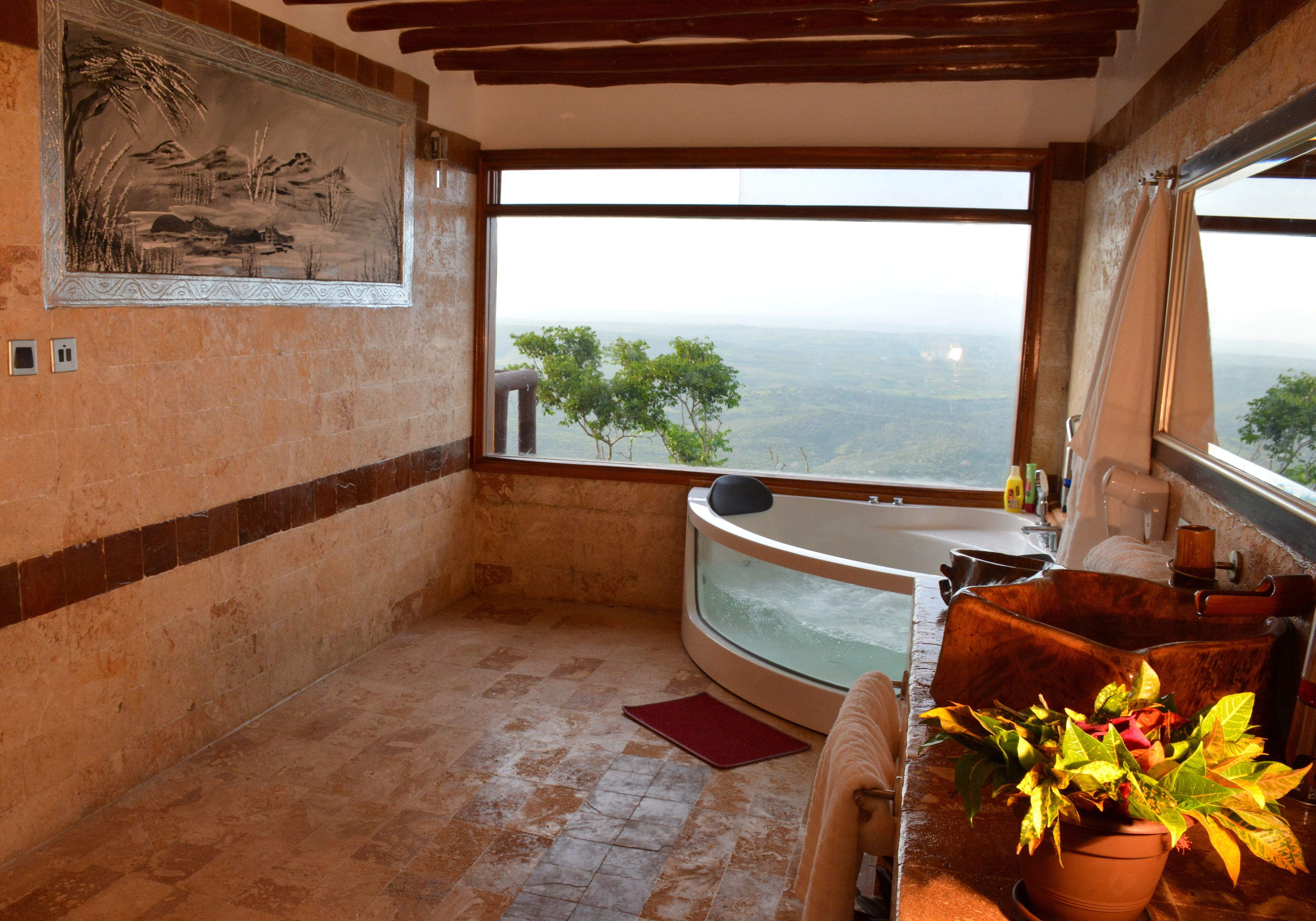 Un baño con bañera, un ventanal con vistas, una planta en maceta y un tapete rojo.