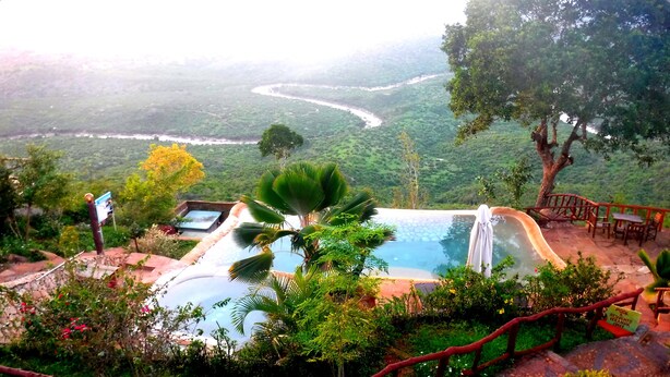 A hot spring area with a pool, surrounded by lush greenery and overlooking a river valley.