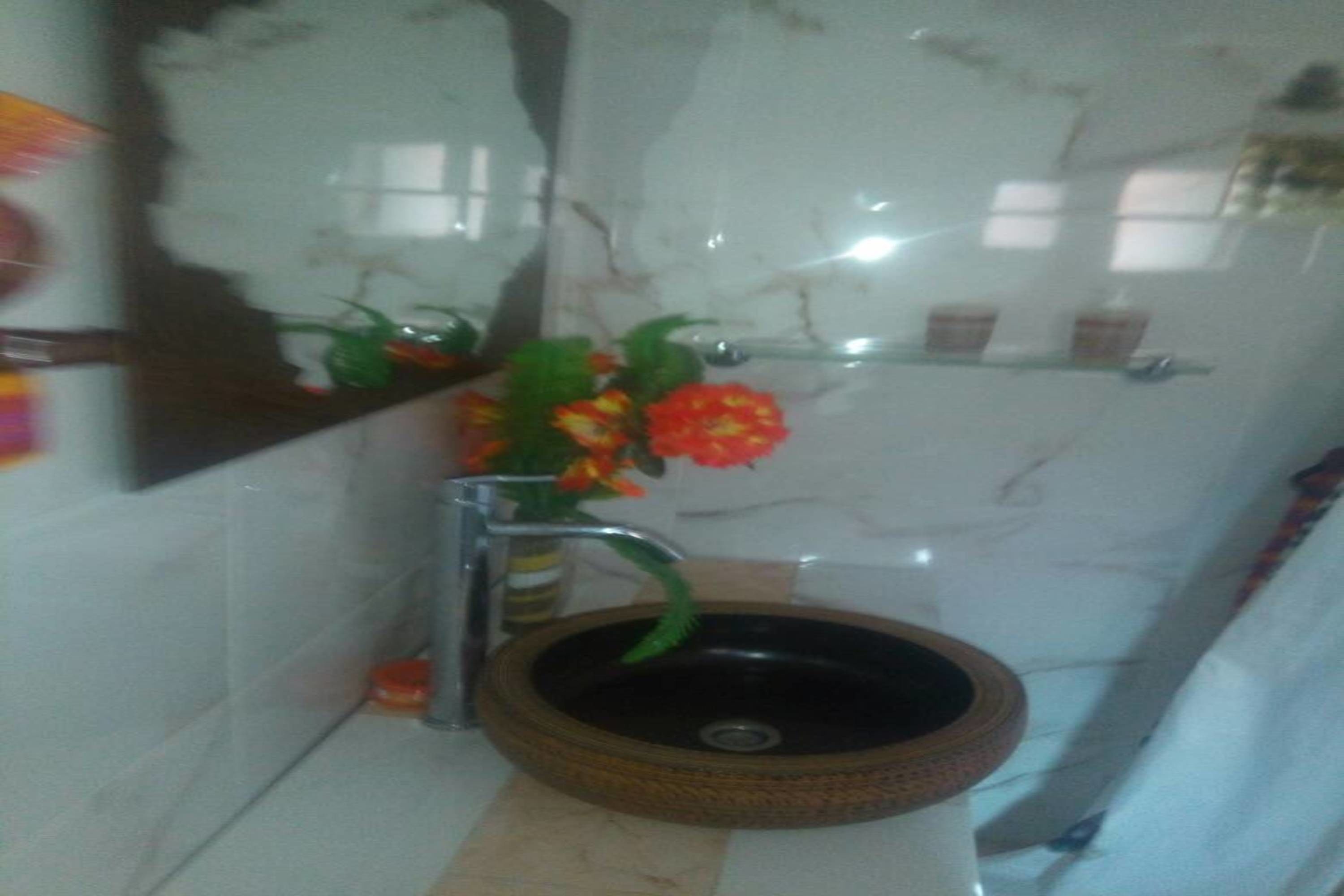 Une salle de bain avec un lavabo rond de couleur marron foncé, un miroir et un vase contenant des fleurs rouges.