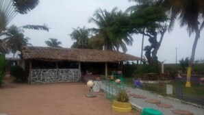 Un edificio rústico con techo de paja, rodeado de palmeras y un camino de grava.