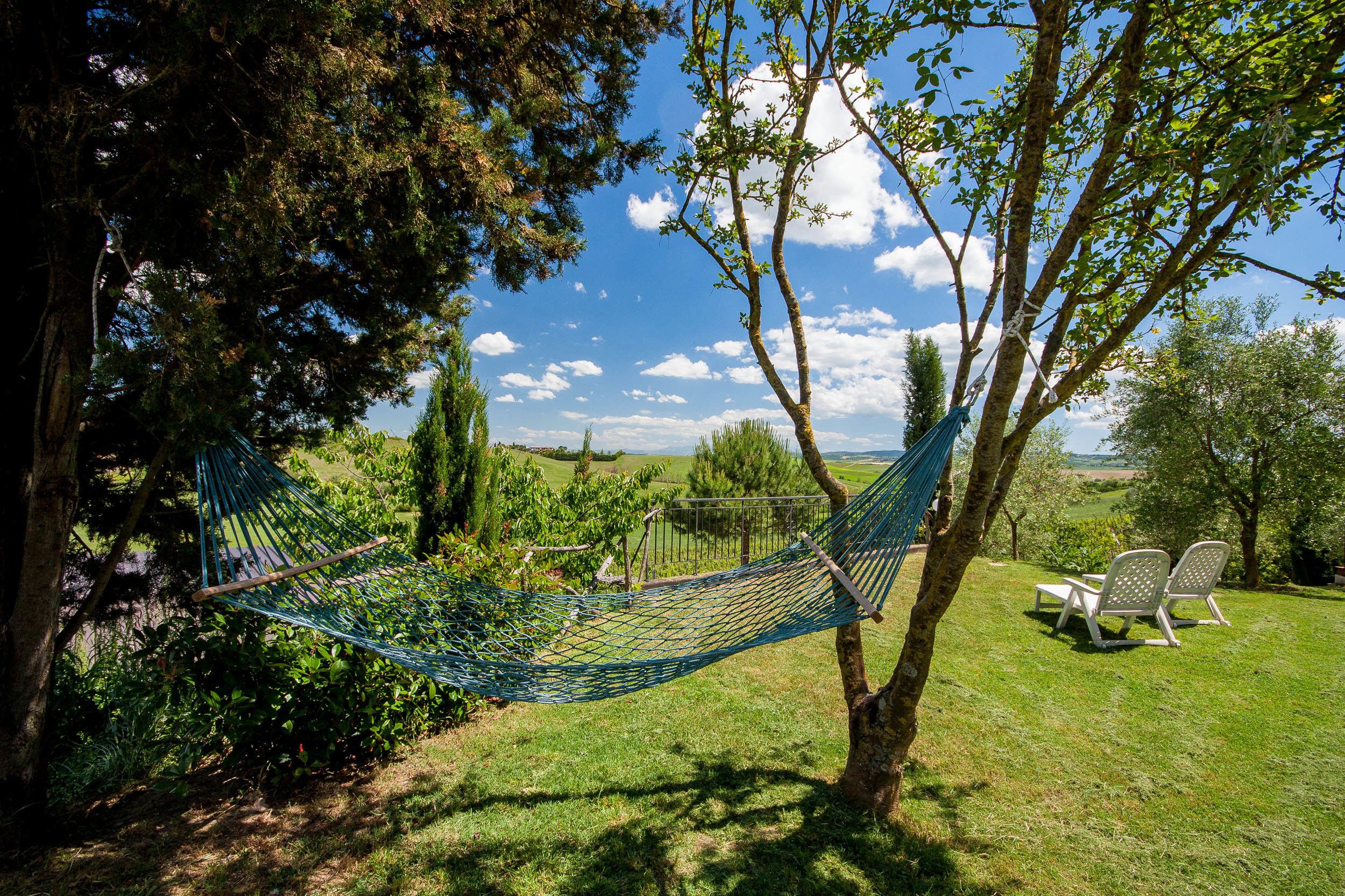 A hammock tied between trees in a grassy area with a view of the countryside.