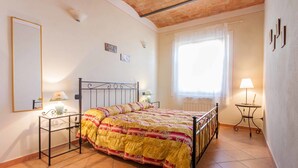 Een slaapkamer met een bed, nachtkastjes, een raam met gordijnen en een betegelde vloer.