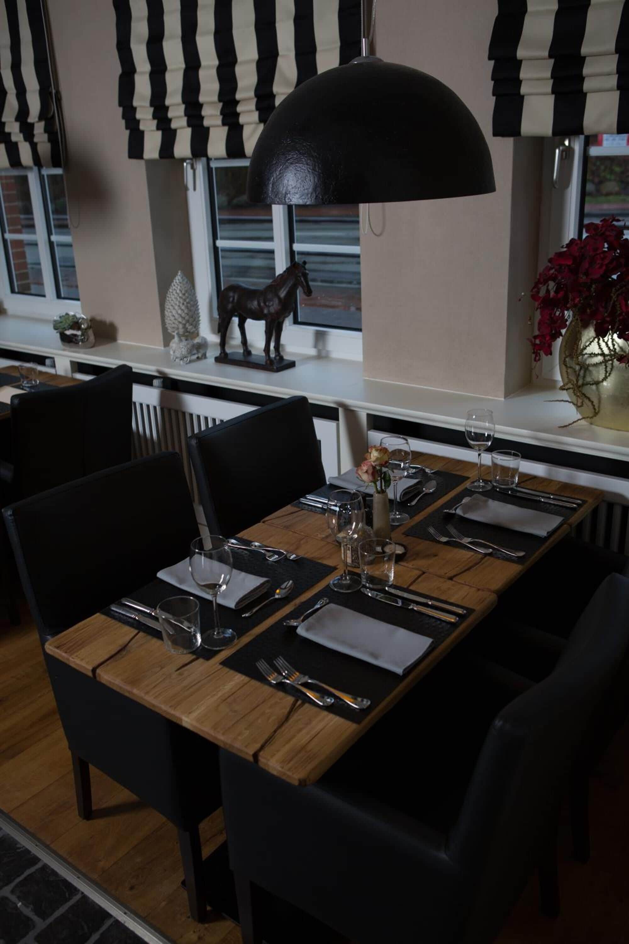 A dining area with a long wooden table set for four, black chairs, and a black pendant light.