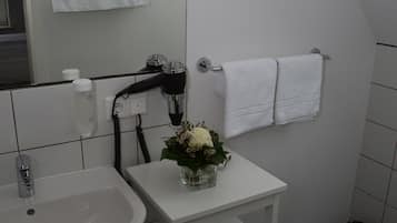 Een moderne badkamer met een witte wastafel, een klein wit wastafelmeubel, een handdoekhouder met twee handdoeken, een haardroger en een prullenbak.