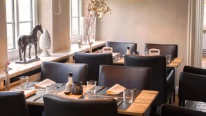 Interior de restaurante con sillas de cuero negro, mesas de madera e iluminación colgante negra.