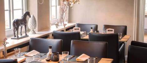 Interior de restaurante con sillas de cuero negro, mesas de madera e iluminación colgante negra.
