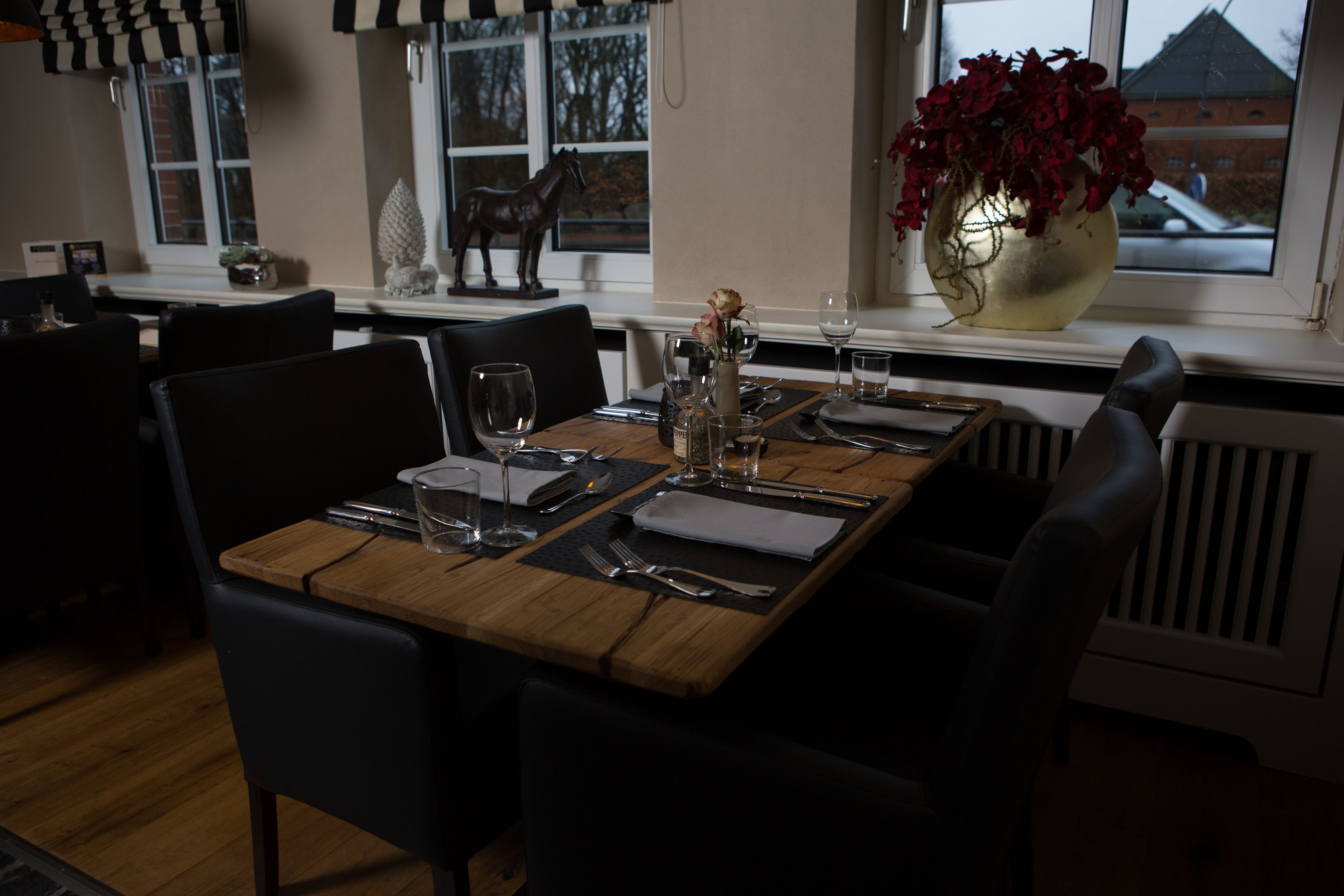 A dining table set with cutlery, glasses, and a vase with flowers.