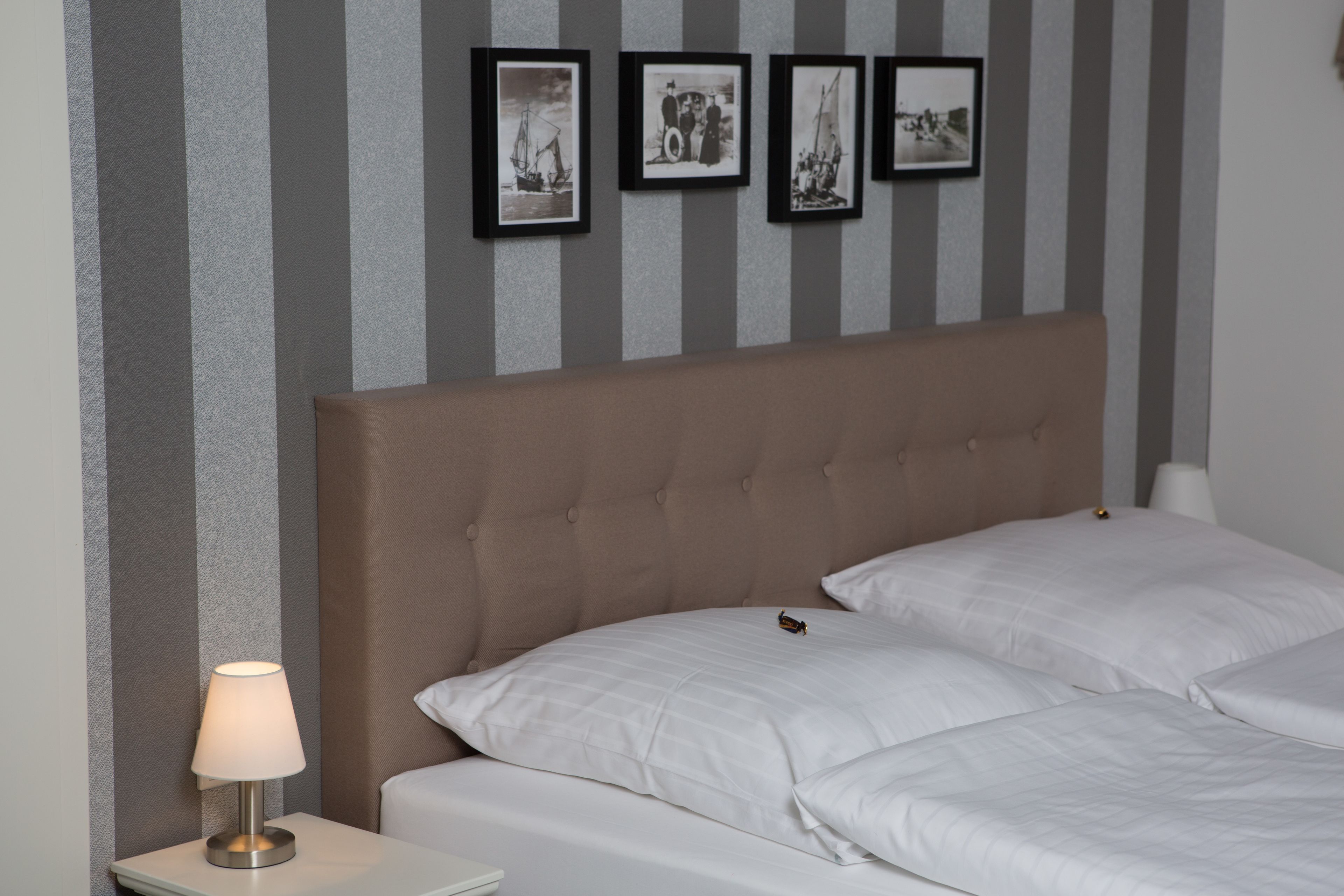 Een netjes opgemaakt bed met witte lakens, een gestoffeerd hoofdbord en een nachtkastje met een lamp.