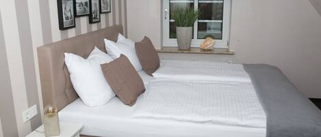 A neatly made bed with a headboard, a bedside table with a lamp, and a window with a view of the outside.