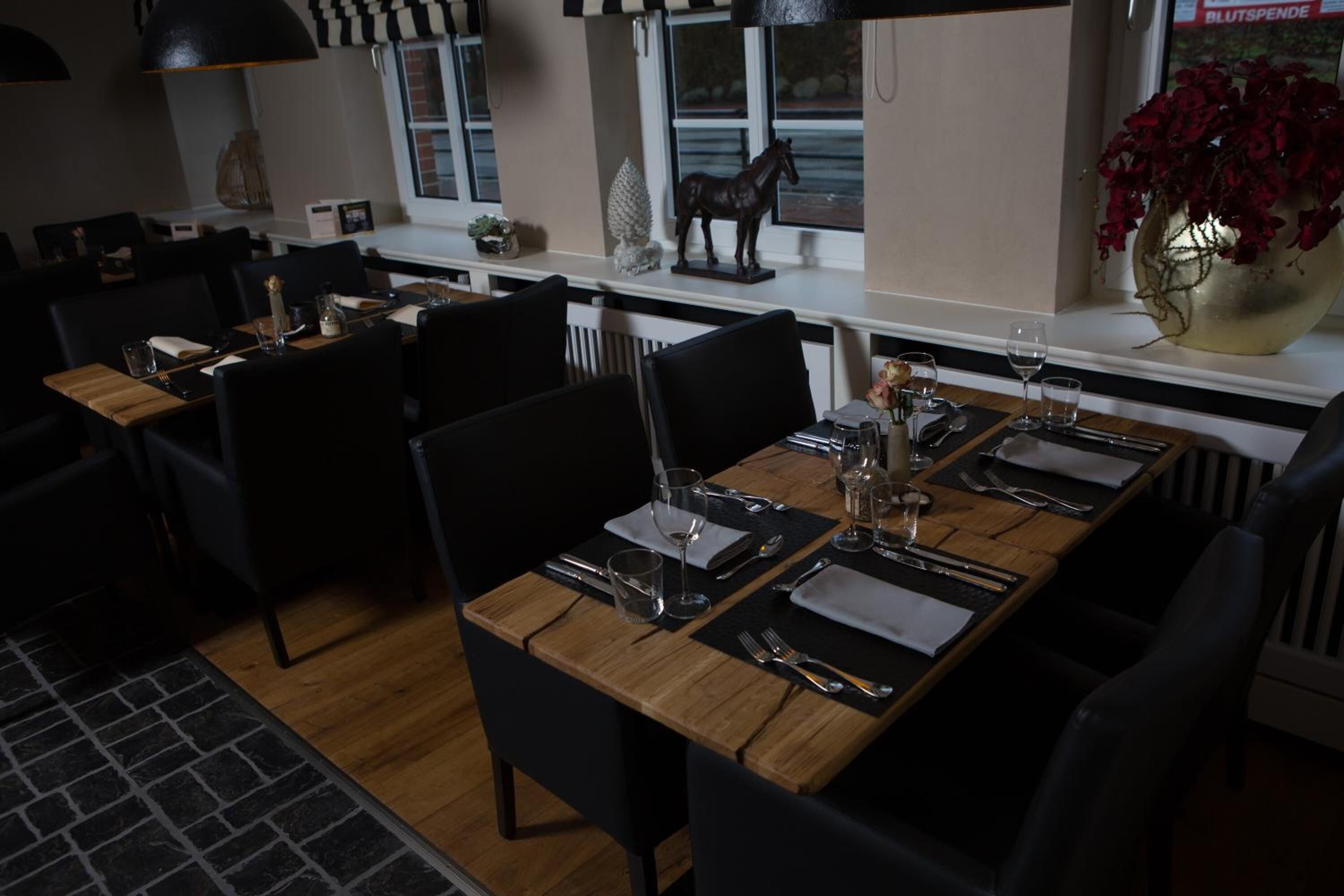 A dining area with a long wooden table set for four, surrounded by black chairs.