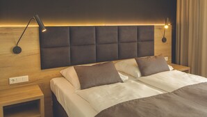 Una habitación de hotel moderna con cabecera de madera, dos mesitas de noche y una cama con ropa blanca y marrón.