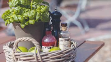 A wicker basket with a potted basil plant, a bottle of red vinegar, and a bottle of olive oil on a wooden table.