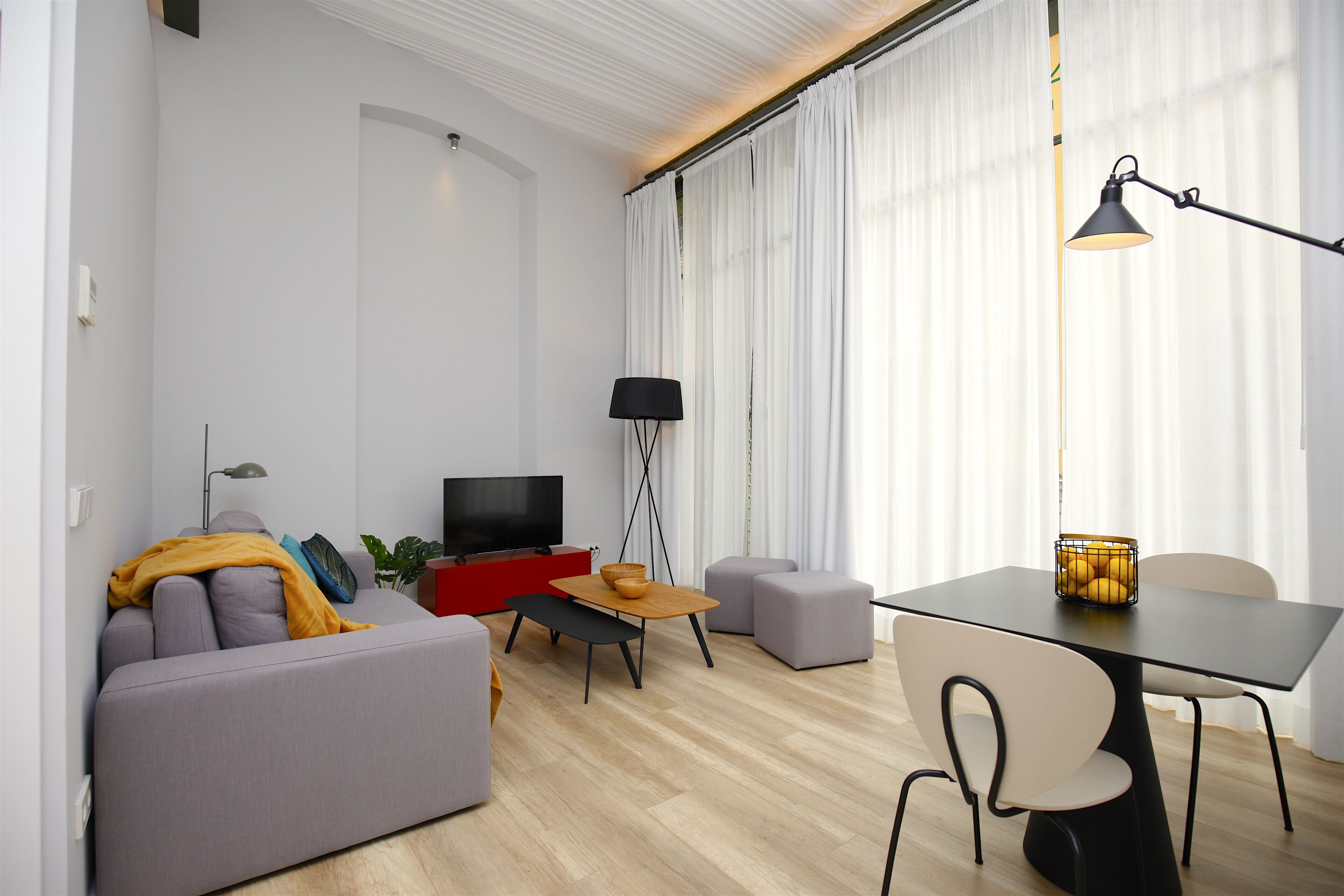 Ein modernes Wohnzimmer mit einer Couch, einer roten Unterhaltungseinheit, einem Esstisch mit Stühlen und einem großen Fenster mit Vorhängen.