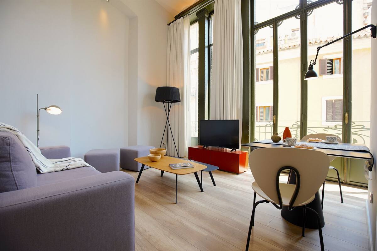Ein modernes Wohnzimmer mit einer Couch, einem Couchtisch, einem Fernseher und einem Essbereich mit einem Stuhl und Tisch.