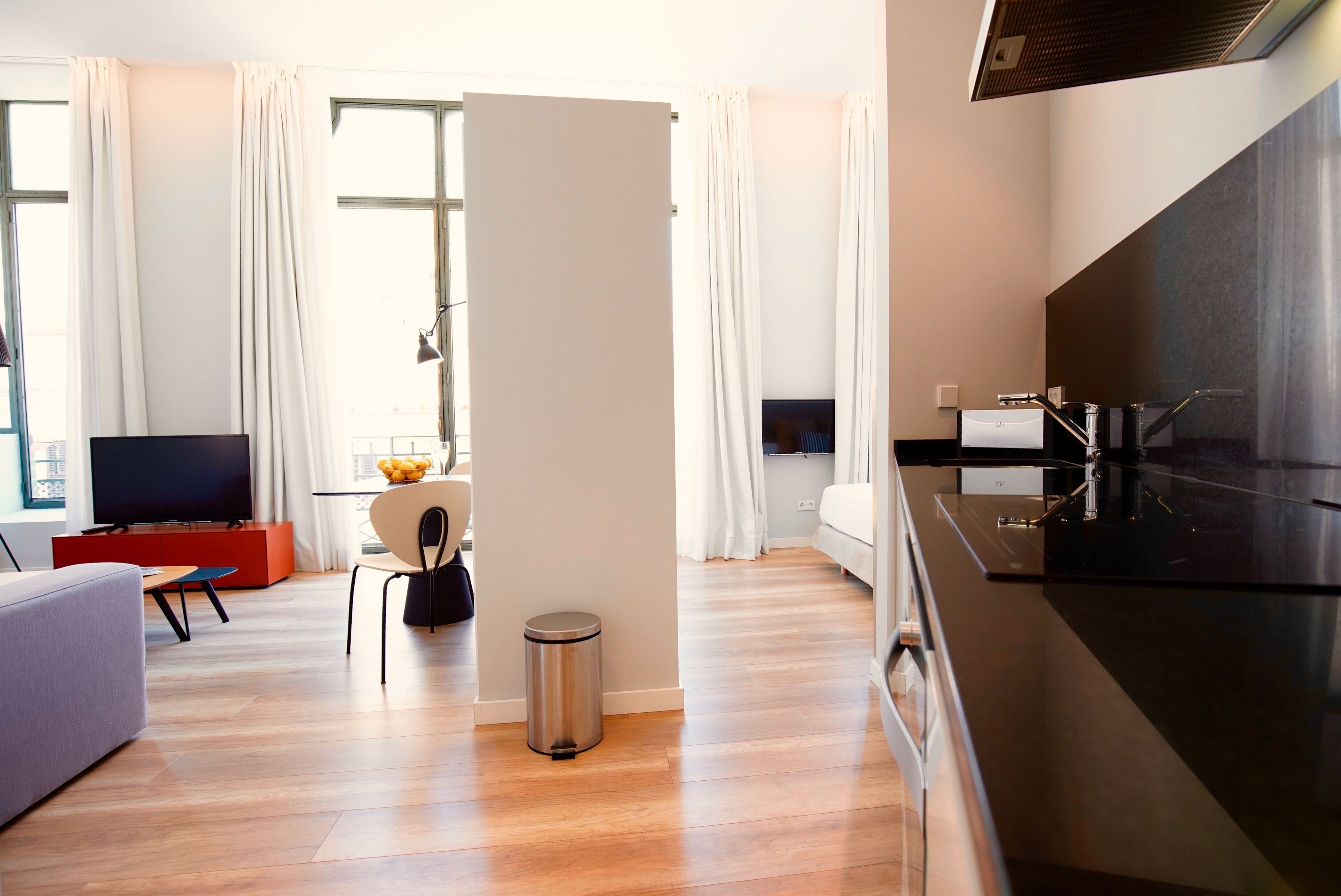 Uma sala de estar moderna com televisão de tela plana, sofá, área de jantar com mesa e cadeiras, e cozinha com fogão.