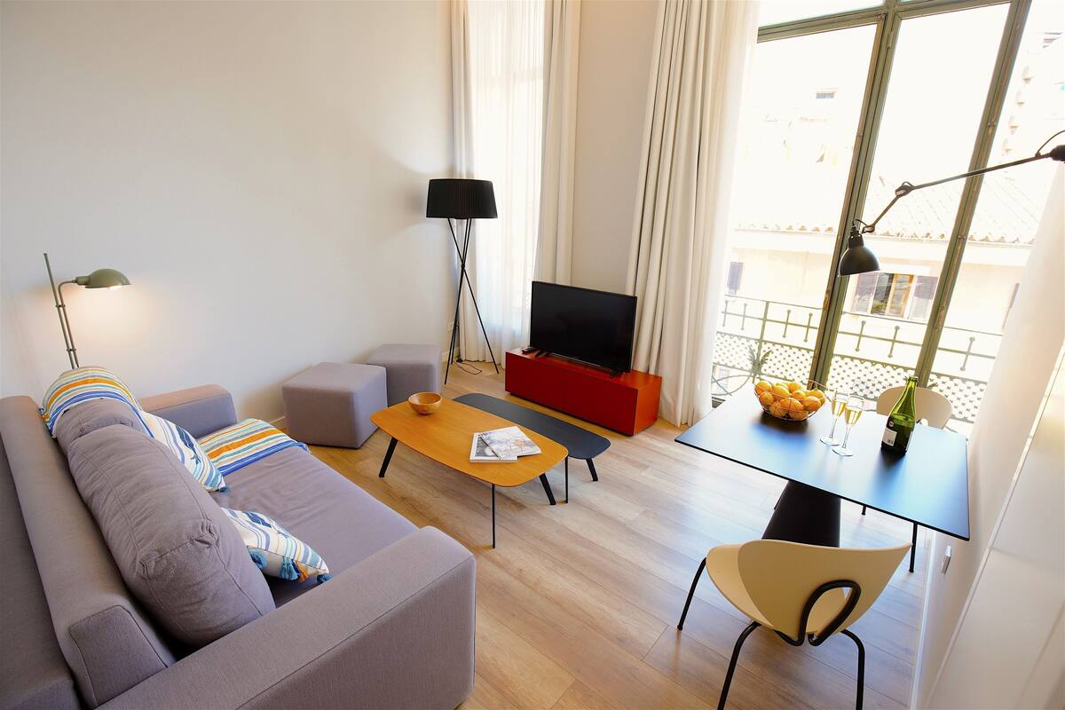 Ein modernes Wohnzimmer mit einer Couch, einem Couchtisch, einem Fernseher und einem Esstisch mit einer Flasche und Gläsern.