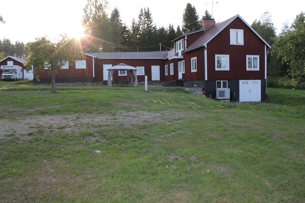 A large red barn with a covered outdoor seating area, a truck, and a grassy field. - Happy Hudiksvall (Hudiksvall)