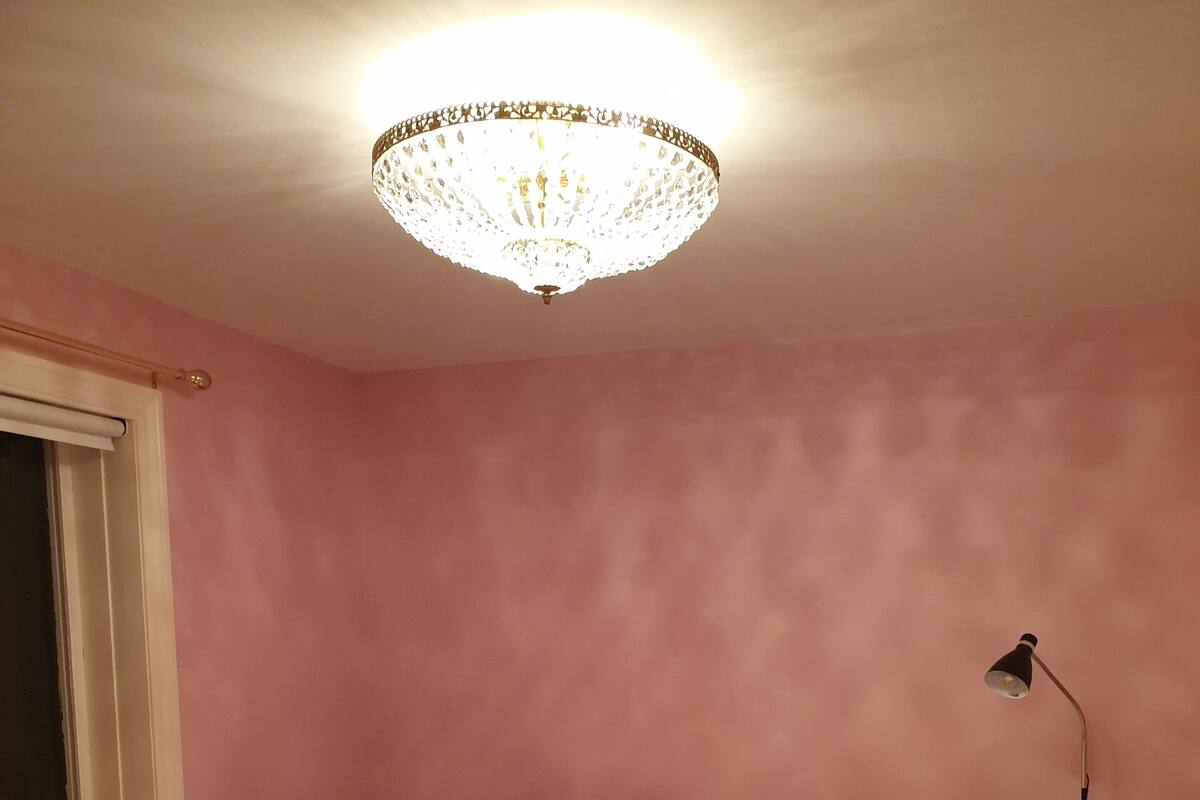 A bedroom with a bed, a window, a lamp, and a chandelier.