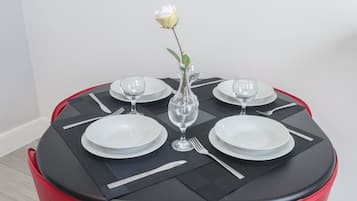 A round dining table with black placemats, white plates, and clear glassware. A single white rose is placed in a clear vase at the center.